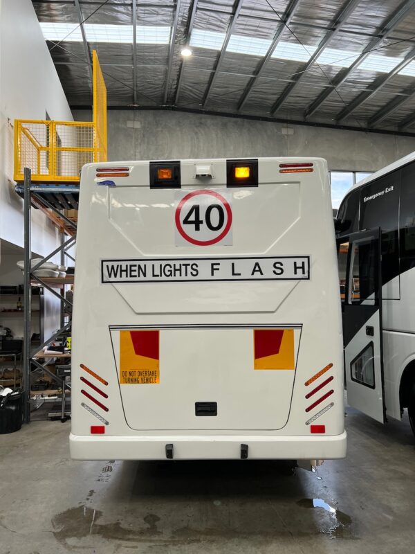 Photo of the rear of a 2024 Isuzu iBus bus with New South Wales TS150 Safebus SB001A surface mount school bus lights and signage